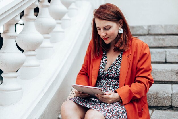 La empresaria en ropa elegante que trabaja utiliza un moderno dispositivo de tableta mientras está sentado en la calle