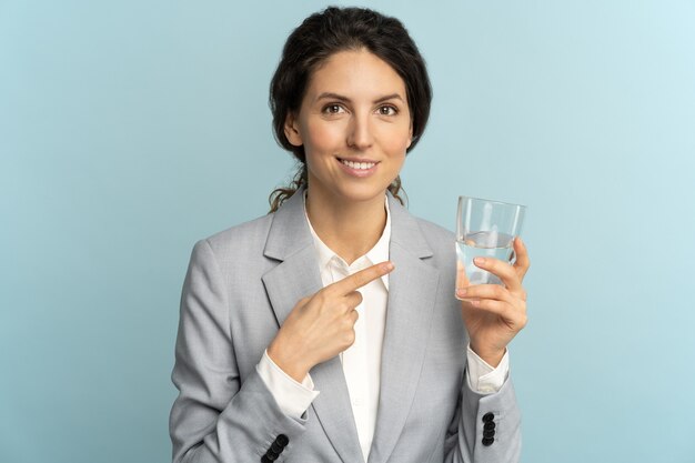 Empresária segurando e mostrando o dedo no copo d'água lembra não se esquecer de beber água no trabalho