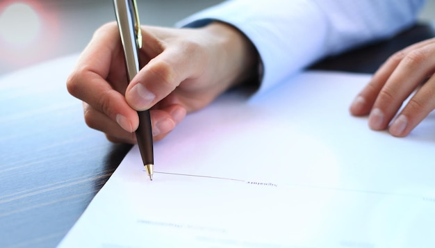 Foto empresária sentada na mesa de escritório assinando um contrato com foco superficial na assinatura