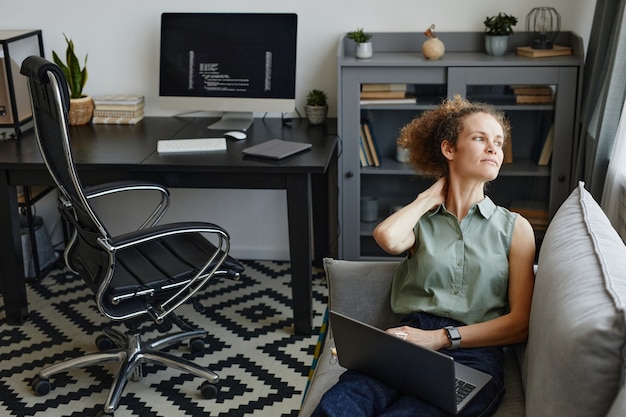 La empresaria sentada en el sofá con el portátil y descansando después de su trabajo en línea en la habitación