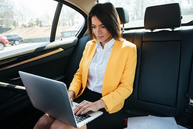 Empresaria sentado en el asiento trasero del coche y trabajando