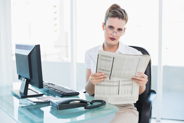 Empresaria seria con gafas sosteniendo un periódico