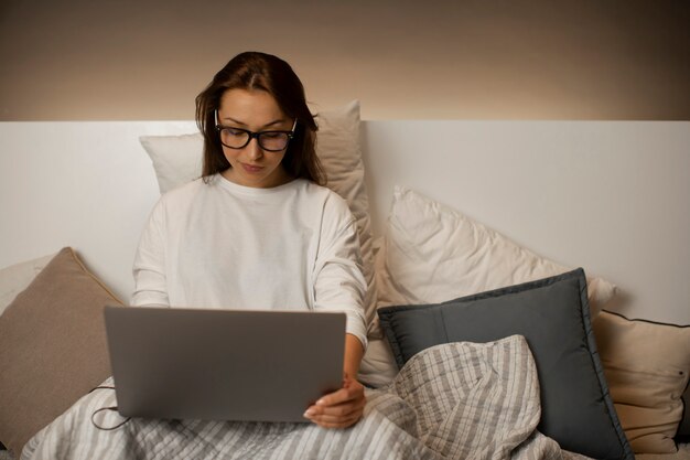 Empresária sexy sentada na cama com o laptop, trabalhando em casa tarde da noite