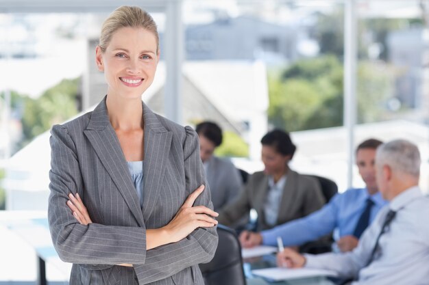 Empresaria sonriendo a la cámara con colegas detrás