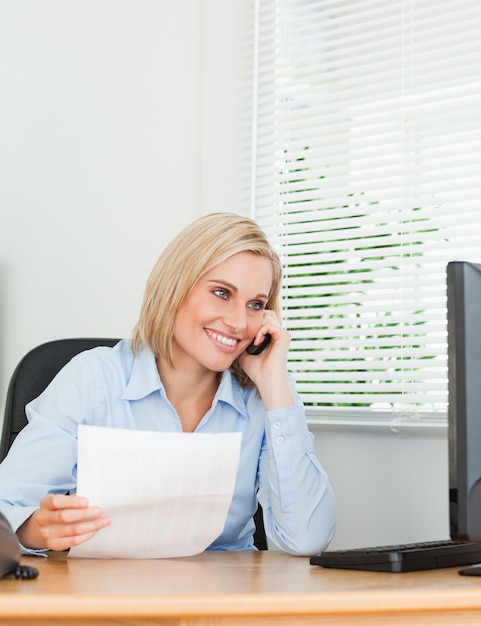 Empresaria sonriendo a la pantalla mientras llamando y sosteniendo un papel