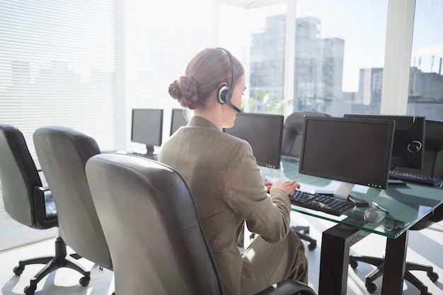 Empresaria sonriente con auriculares usando computadoras