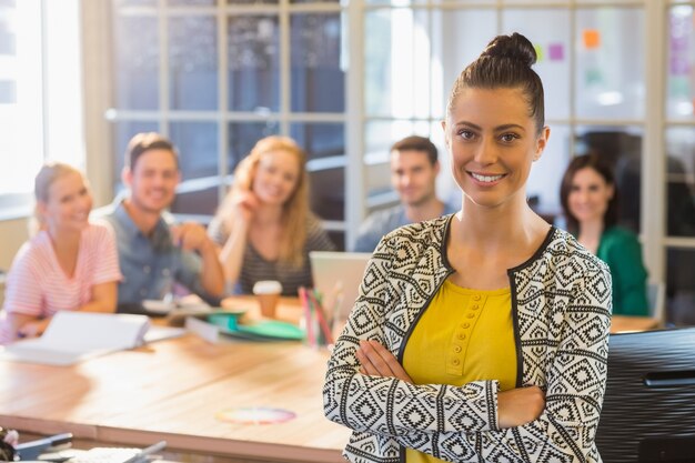 Empresaria sonriente con colegas en segundo plano en la oficina