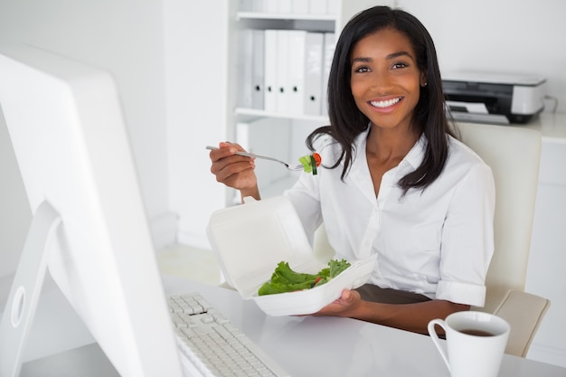 Empresaria sonriente comiendo una ensalada en su escritorio