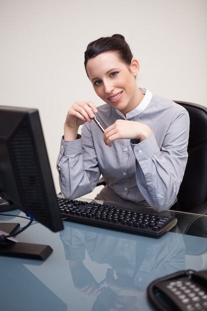 Empresaria sonriente con la pluma que se sienta en su escritorio