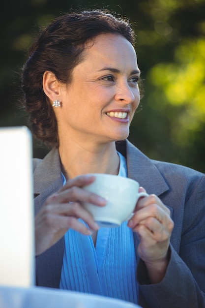 Empresaria sonriente que bebe el café con la computadora portátil