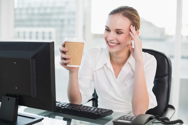 Empresaria sonriente que sostiene la taza disponible que se sienta en el escritorio