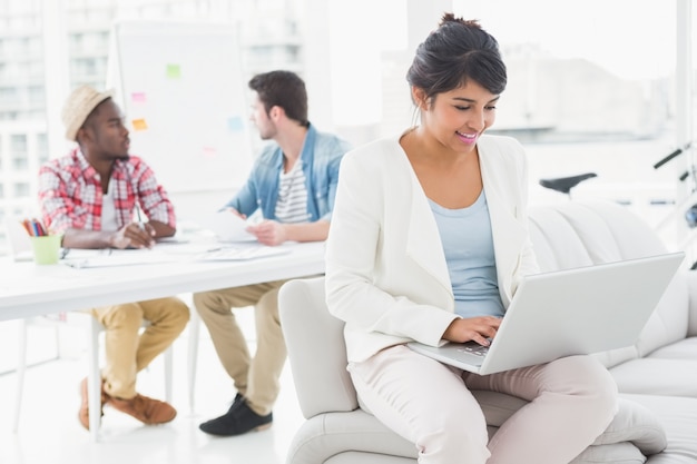 Empresaria sonriente que usa la computadora portátil en el sofá