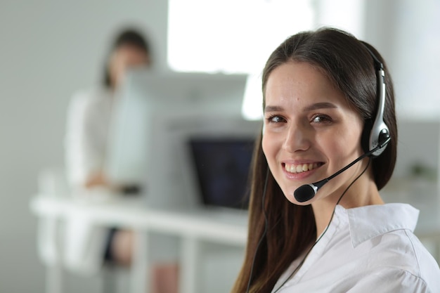 Empresaria sonriente u operador de línea de ayuda con auriculares y computadora en la oficina
