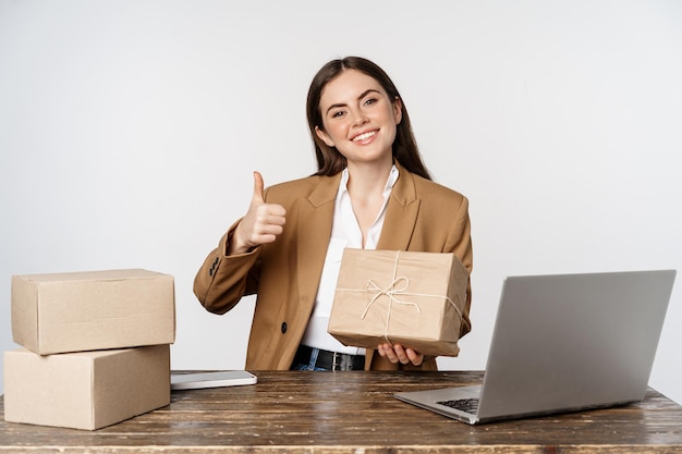 Empresária sorridente mostrando pedidos de pacotes em caixas e polegares para cima trabalhando em seu próprio...