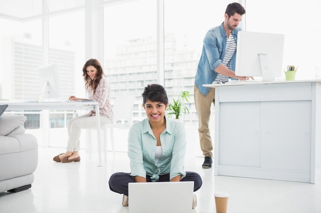 Empresária sorridente sentada no chão usando laptop