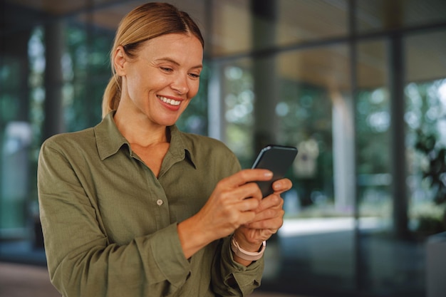 Empresária sorridente usando o telefone em pé no fundo do edifício moderno