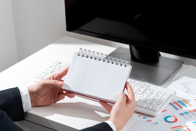 Empresaria sosteniendo un cuaderno con nuevas ideas sobre el escritorio con computadora y teclado Mujer en traje con bloc de notas con mensajes importantes sobre la mesa de la oficina