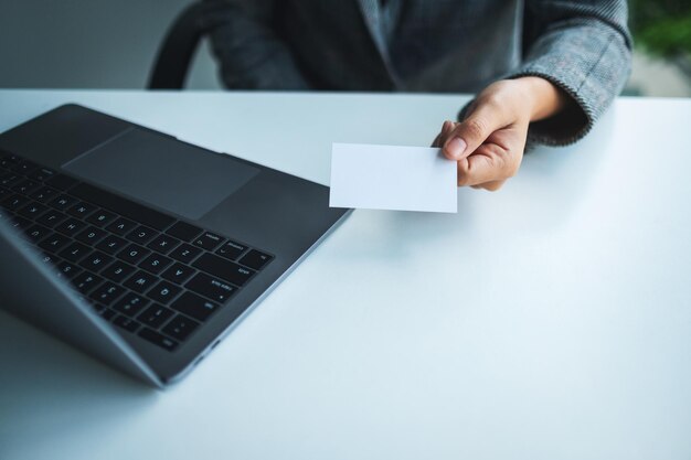 Una empresaria sosteniendo y dando tarjetas en blanco mientras usa una computadora portátil en la oficina