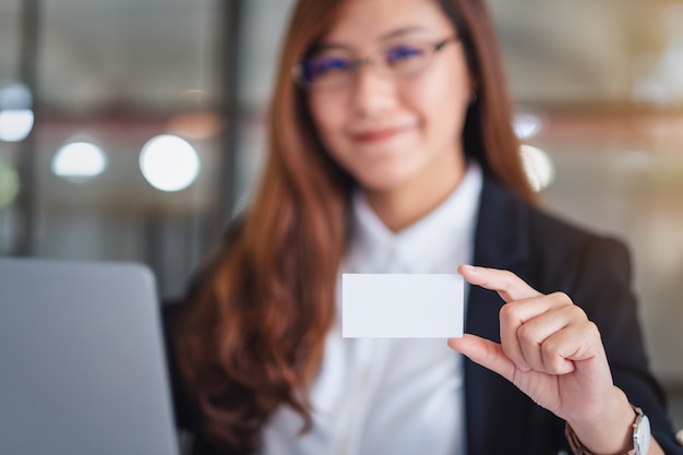 Foto una empresaria sosteniendo y mostrando una tarjeta de presentación en blanco mientras usa una computadora portátil en la oficina