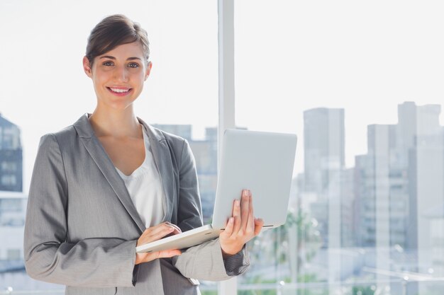 Foto empresaria sosteniendo portátil y sonriendo a la cámara