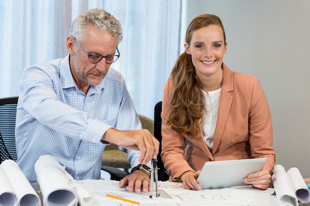 Empresaria sosteniendo tableta digital mientras compañero de trabajo trabajando en plano con brújula