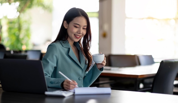 Empresaria sosteniendo una taza de café y analizando datos comerciales en línea en una computadora portátil.