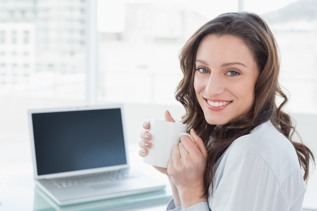 Empresaria con taza de café en frente de la computadora portátil en la oficina