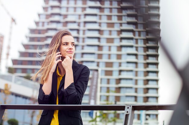 Empresaria con un teléfono móvil en la calle con edificios de oficinas