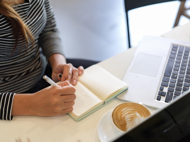 La empresaria trabaja durante la pausa para el café en la cafetería, computadora portátil, taza de café en la mesa