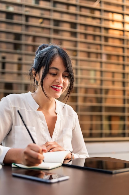 Empresaria trabajando y tomando notas en la terraza de una cafetería, concepto de emprendedor digital y estilo de vida urbano, copia espacio para texto