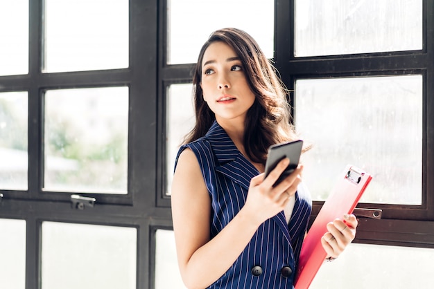 Empresaria trabajando y usando el teléfono móvil mientras está de pie en la oficina