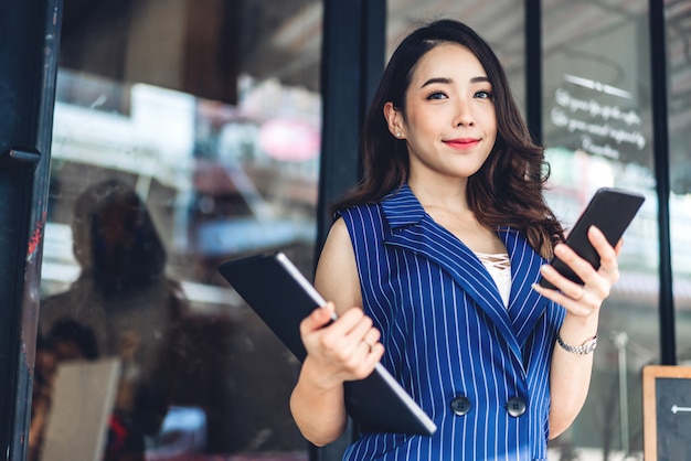 Empresaria trabajando y usando el teléfono móvil mientras está de pie delante del café