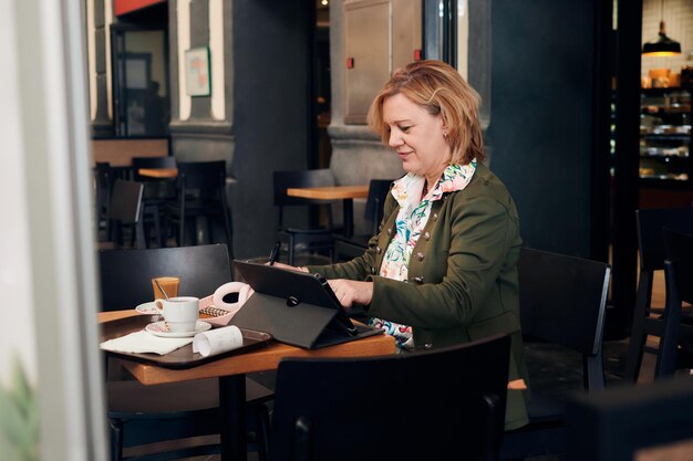 Empresária trabalhando na cafeteria com um tablet e um notebook