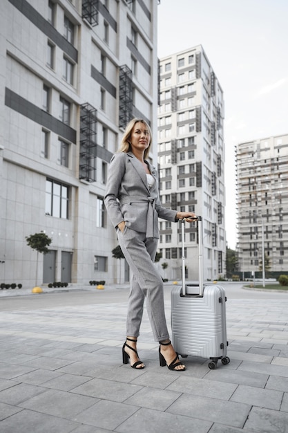 La empresaria en traje gris en viaje de negocios caminando con su equipaje en la ciudad