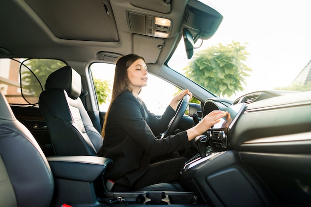 La empresaria en traje negro se sienta al volante de un automóvil premium y mira el monitor del sistema de navegación