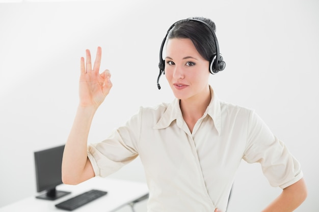 Empresaria usando auriculares mientras gesticula bien firmar en la oficina