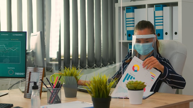 Foto empresaria con visera y máscara de protección trabajando en la nueva oficina comercial normal. freelancer discutiendo con un colega en una empresa financiera sobre el respeto a la distancia social durante una pandemia global.