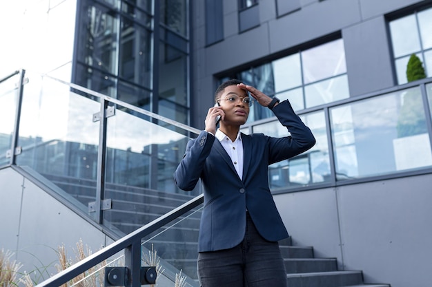 Empresária zangada e séria falando ao telefone fora do escritório Mulher afro-americana vestida com roupas de negócios se comunicando com colegas