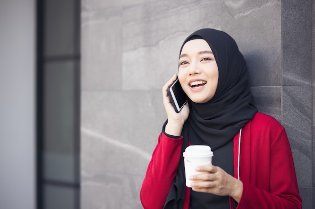 Empresarias árabes en hijab sosteniendo un café en la calle y sosteniendo un teléfono celular