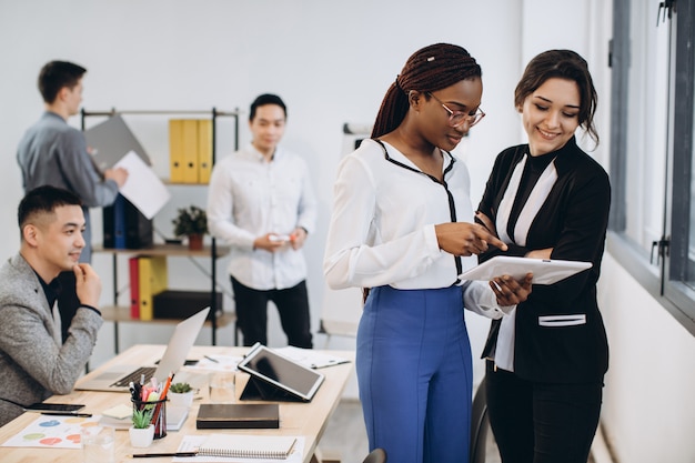 Empresarias blancas africanas y caucásicas que usan una tableta con un grupo interracial de hombres de negocios