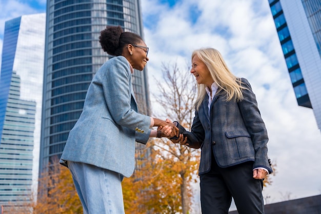 Empresarias y ejecutivas multiétnicas sonriendo y saludando dándose la mano en un parque empresarial