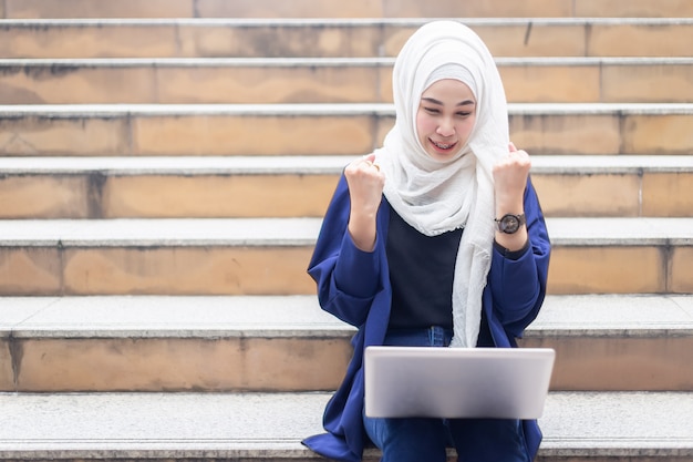 Empresarias musulmanas felices en hijab con laptop trabajando al aire libre.