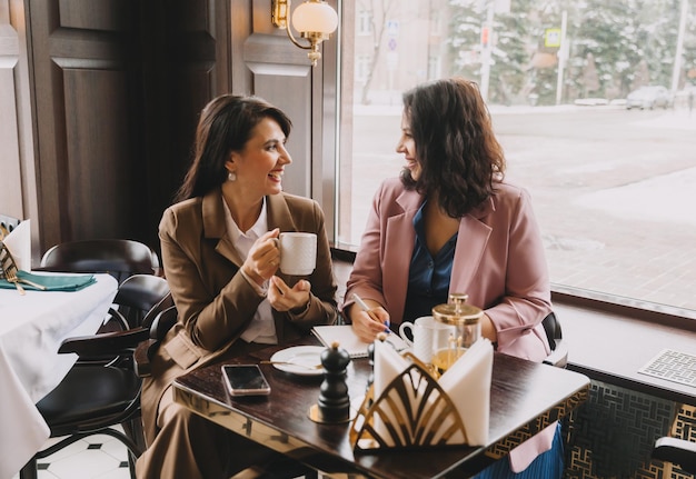 Foto empresárias sentam-se em um café bebem café e conversam sobre negócios, discutem negócios e se divertem