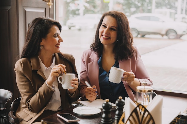 Empresárias sentam-se em um café bebem café e conversam sobre negócios, discutem negócios e se divertem