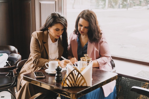 Empresárias sentam-se em um café bebem café e conversam sobre negócios, discutem negócios e se divertem