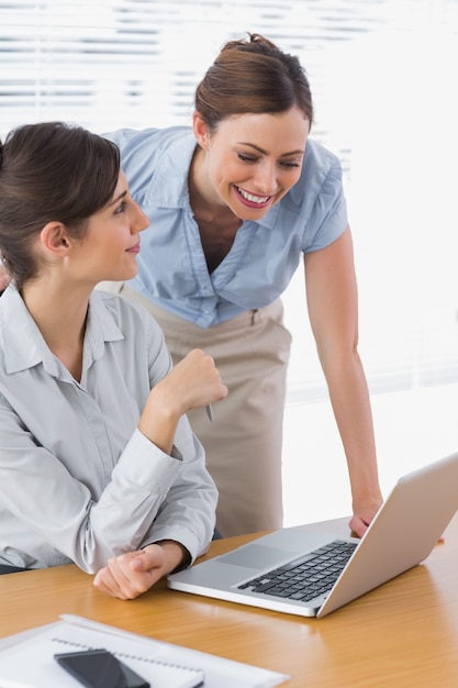 Empresárias sorridentes trabalhando em conjunto com laptop