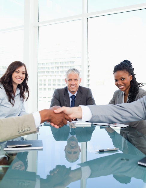 Empresárias sorrindo durante uma reunião ao olhar colegas apertando as mãos