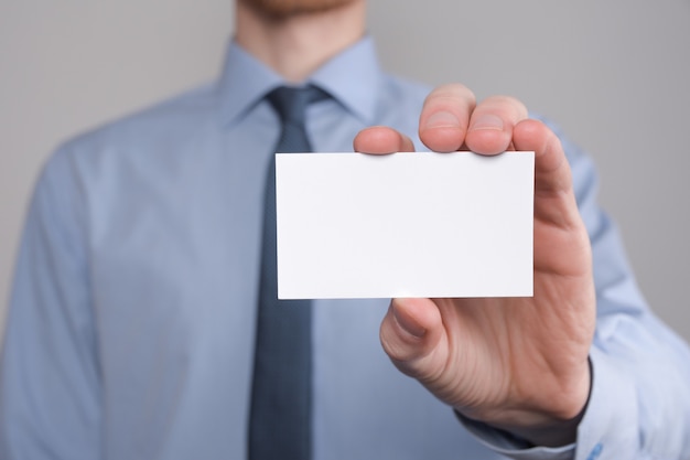 Empresário, a mão do homem de negócios segura apresentando cartão de visita - close-up filmado em fundo cinza. mostre um pedaço de papel em branco. cartão de visita em papel.