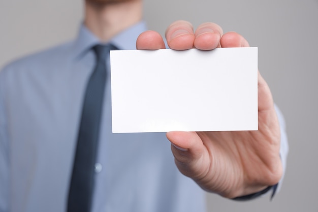 Empresário, a mão do homem de negócios segura apresentando cartão de visita - close-up filmado em fundo cinza. mostre um pedaço de papel em branco. cartão de visita em papel.