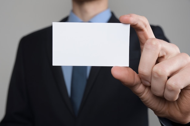 Empresário, a mão do homem de negócios segura apresentando cartão de visita - close-up tiro na parede cinza. Mostre um pedaço de papel em branco. Cartão de visita em papel.